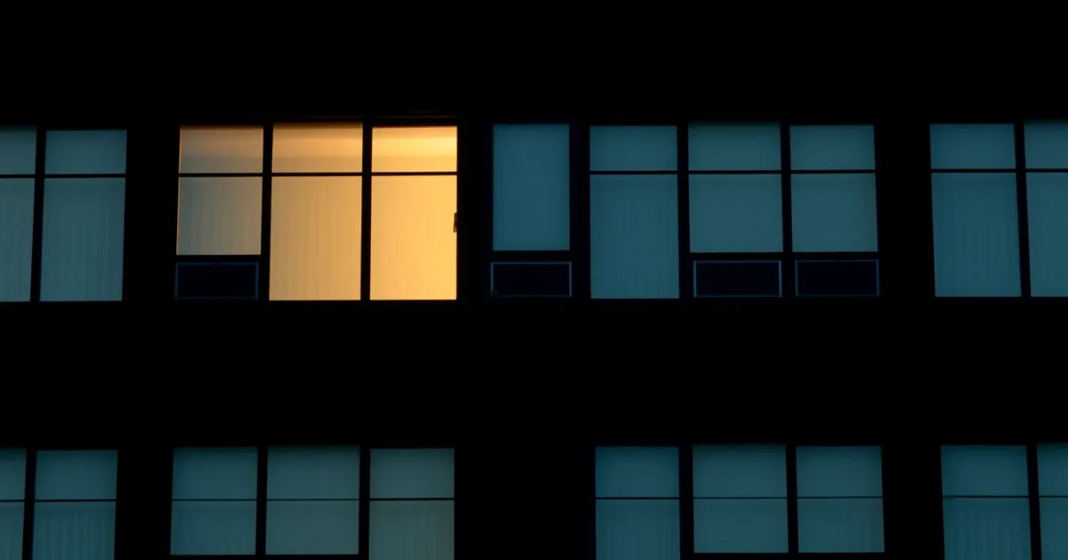 A dark facade of identical windows, a few lit from within, illustrating supporting parents abroad: the tax rules